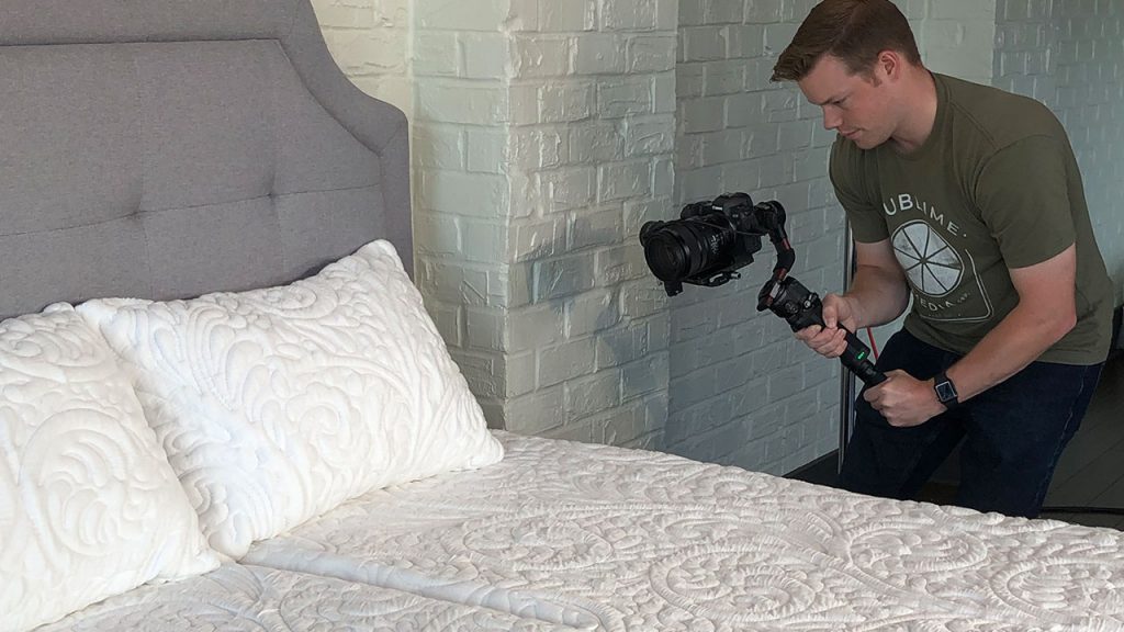 Videographer capturing footage of a pillow on a Posh + Lavish mattress during a product video shoot