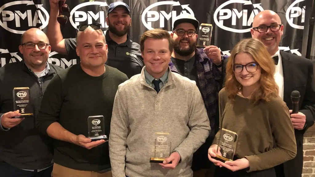 Sublime Media Group team at PMA Markie Awards holding trophies in front of a PMA curtain