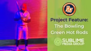 A baseball player stands in front of a garage door lit red and blue. Text reads "Project Feature: The Bowling Green Hot Rods"