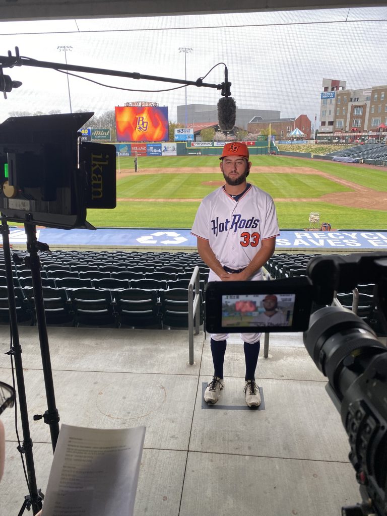 A baseball player stands in front of a field. The view is from behind a camera.