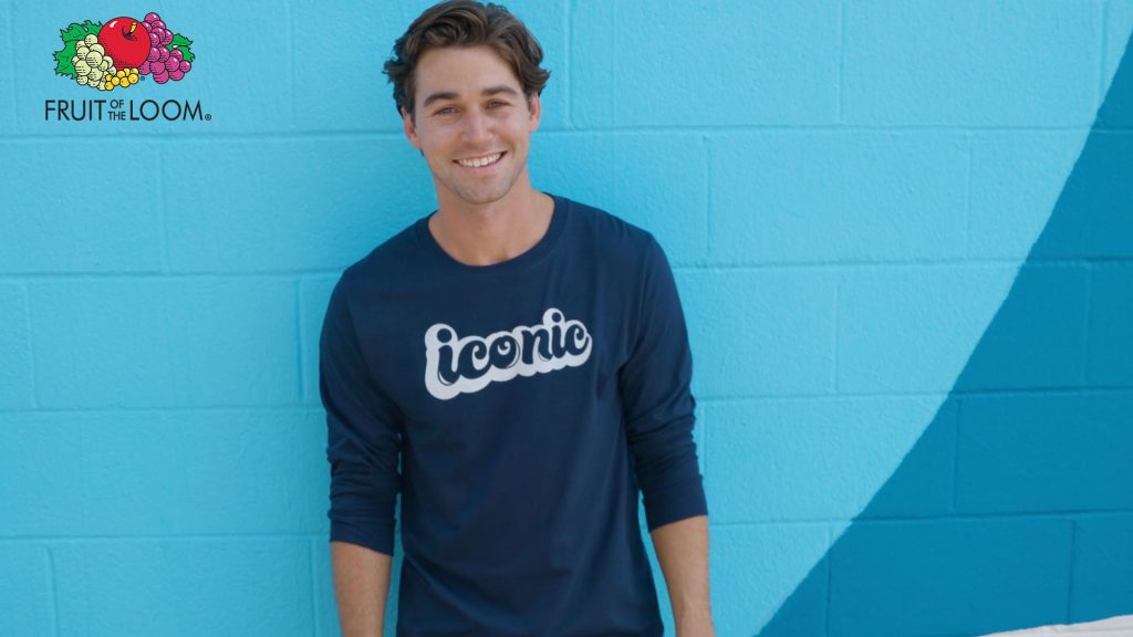 Fruit of the Loom logo and adult male wearing a navy blue Iconic Tee Shirt in front of a light blue wall