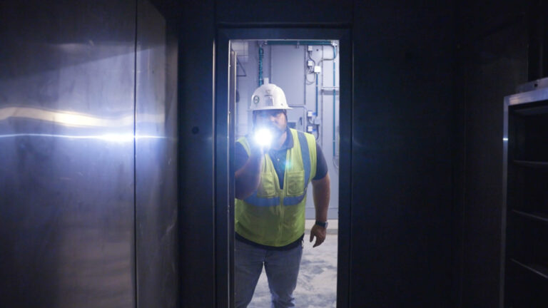 A worker is shining a flashlight in an HVAC unit causing a lens flare on the camera